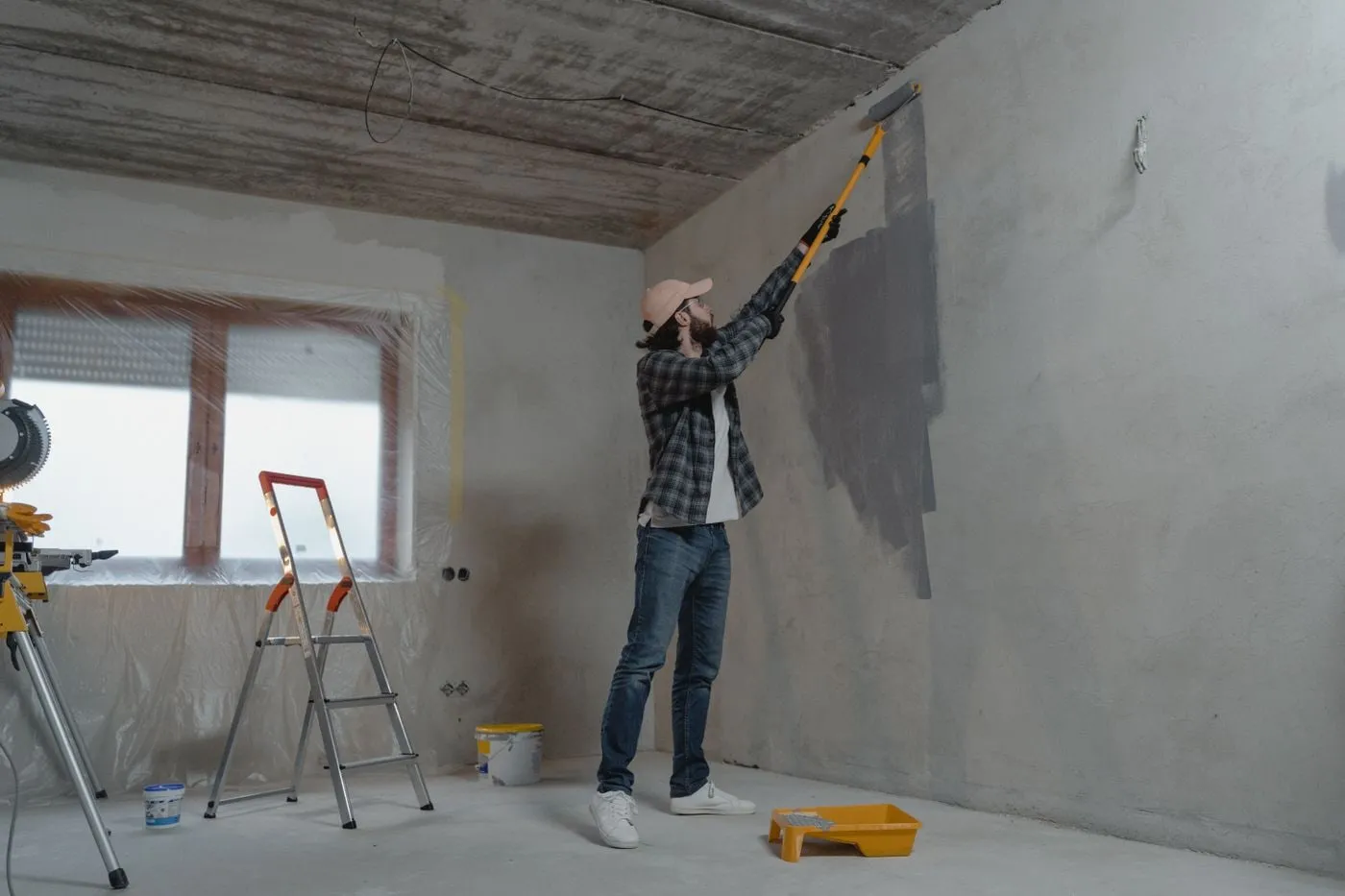 Pintor aplicando pintura con rodillo de mango largo en la pared de una vivienda